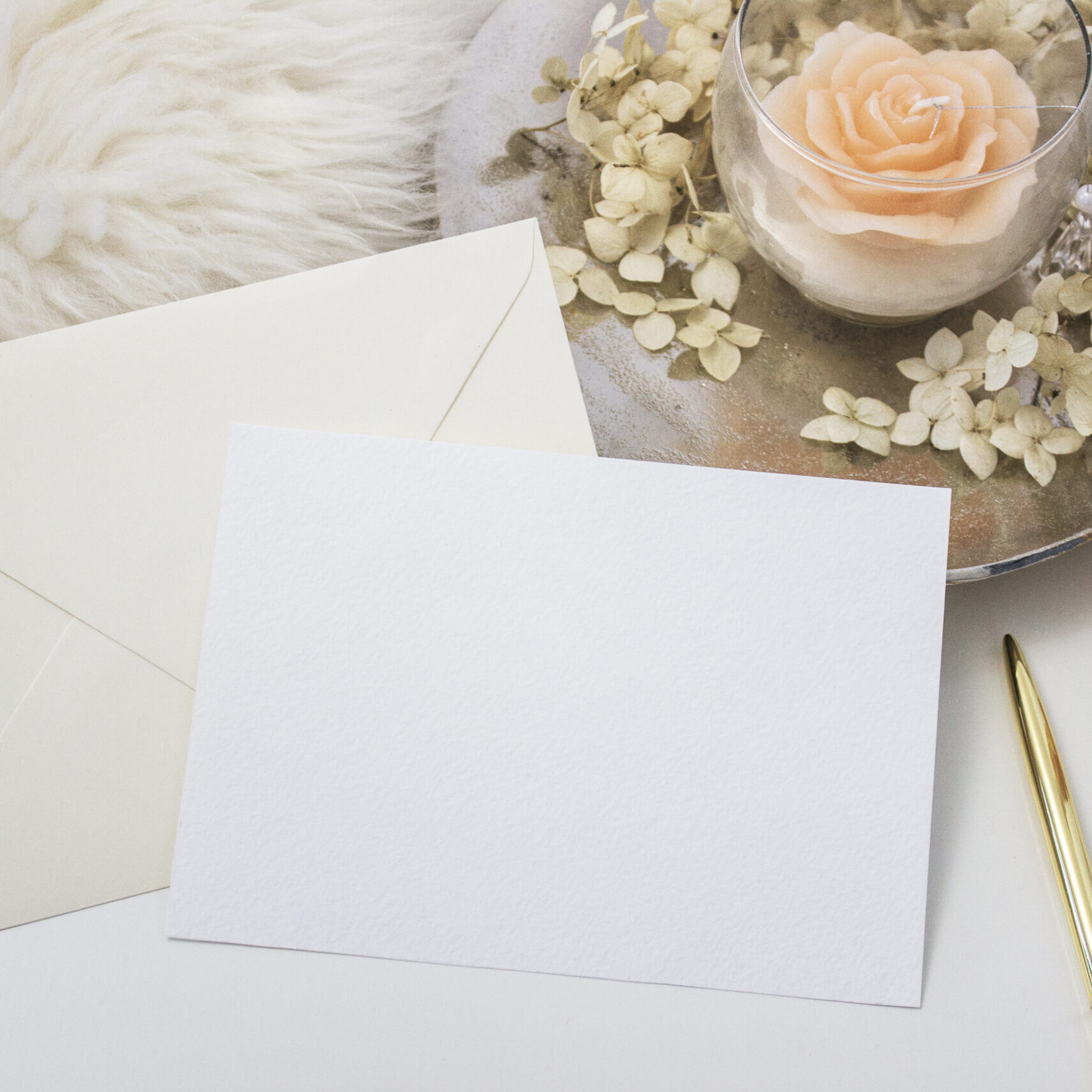 Elegant feminine stationery mockup scene with a blank paper greeting card, golden accessories, candle and flowers, on white background.